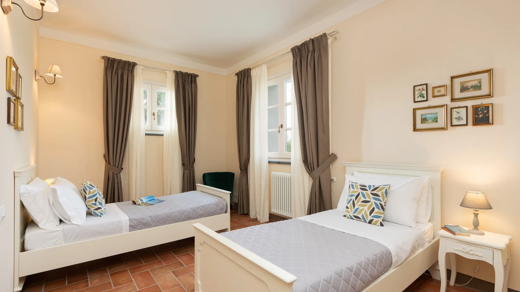 Un dormitorio con dos camas, ventanas con cortinas y cuadros en la pared.