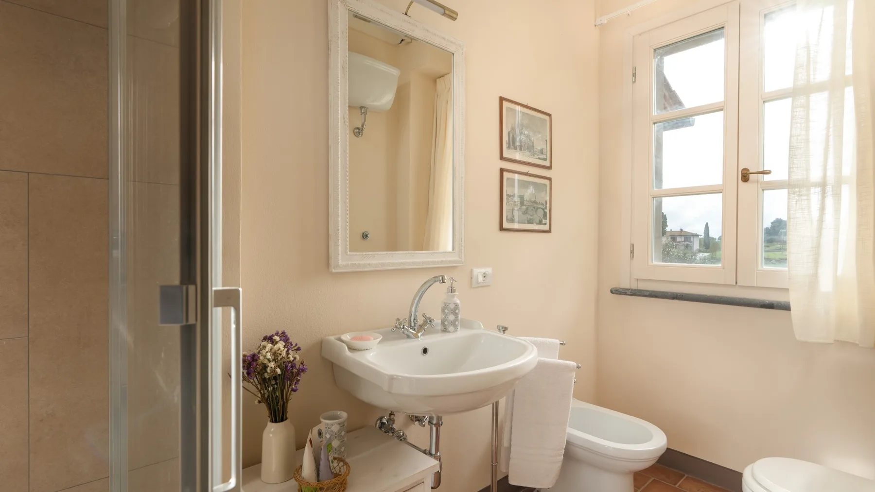 Un baño con lavabo, inodoro y ducha de vidrio junto a una ventana.