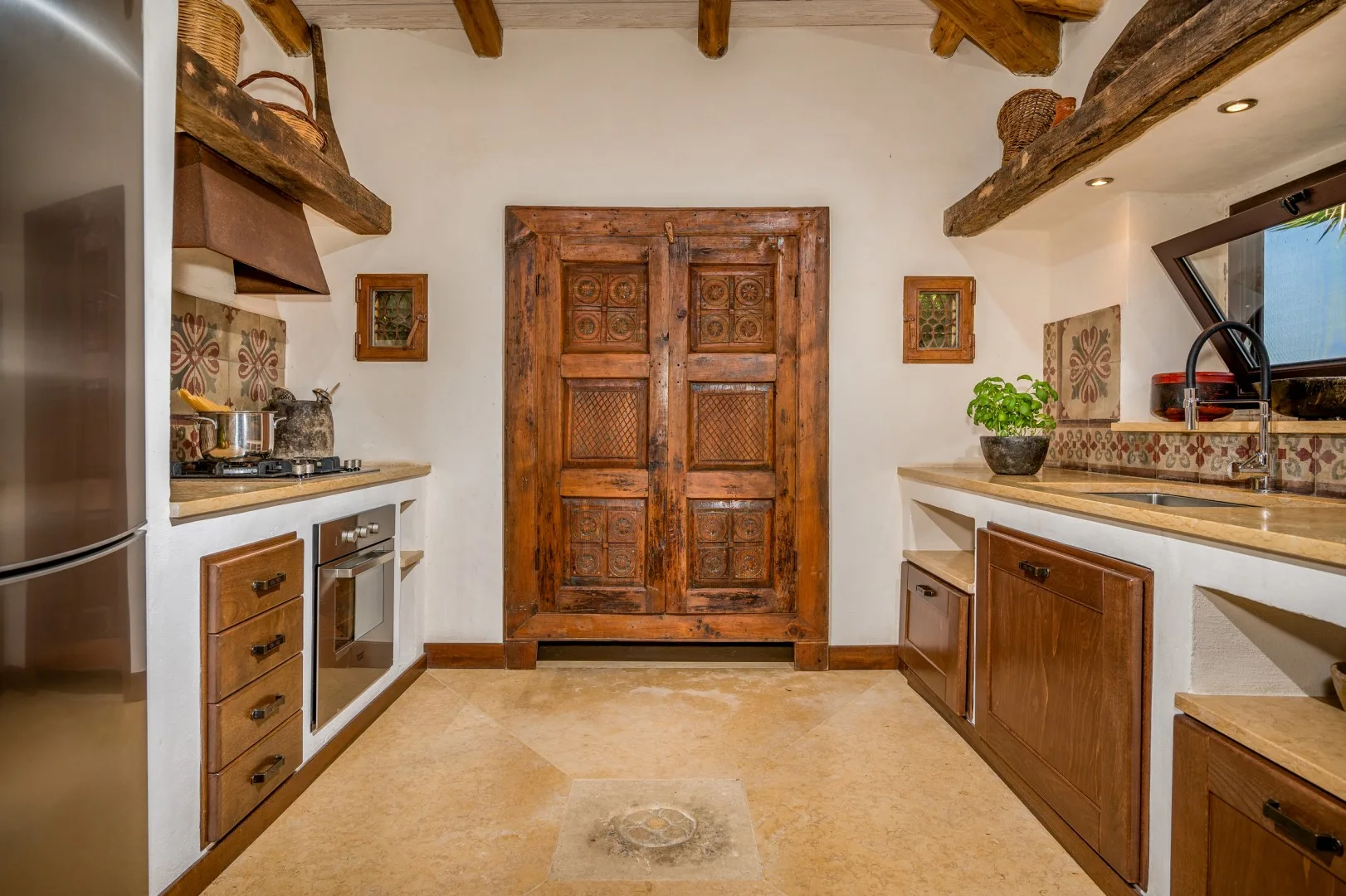 Una cocina con gabinetes de madera, una puerta tallada en el centro y vigas expuestas en el techo.