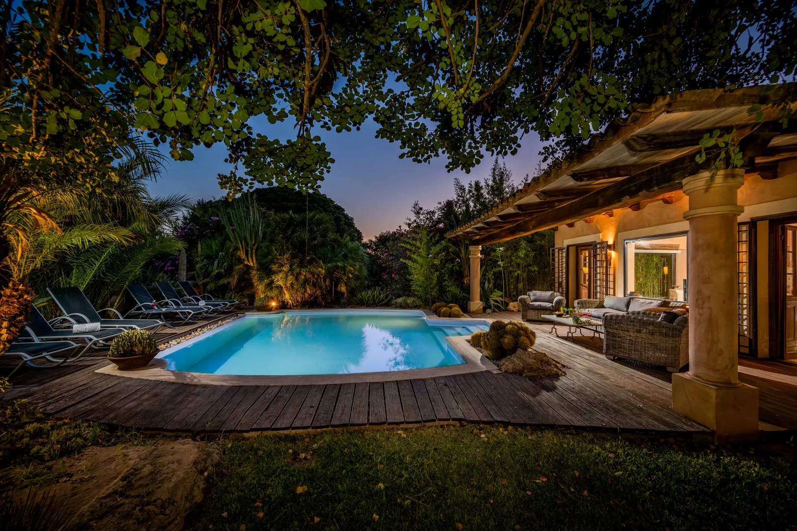 Una piscina al aire libre está junto a una terraza de madera y un patio iluminado.