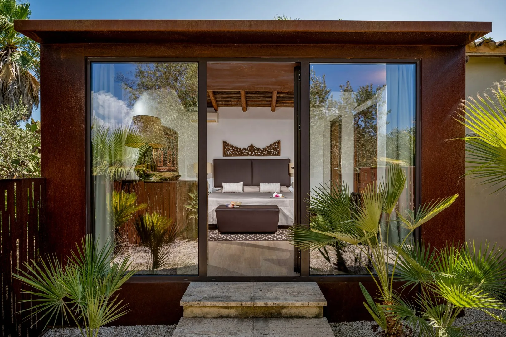 Dormitorio visto a través de puertas corredizas de vidrio, con una cama y plantas.