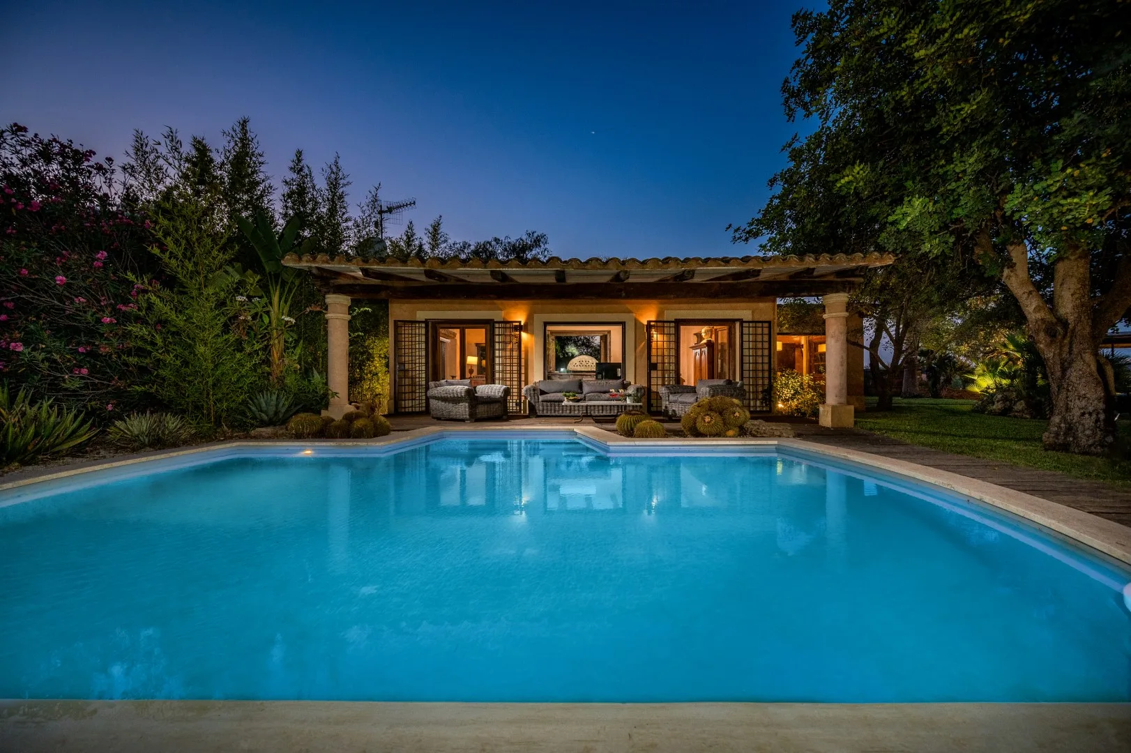 Una piscina frente a una zona de estar exterior iluminada al anochecer.