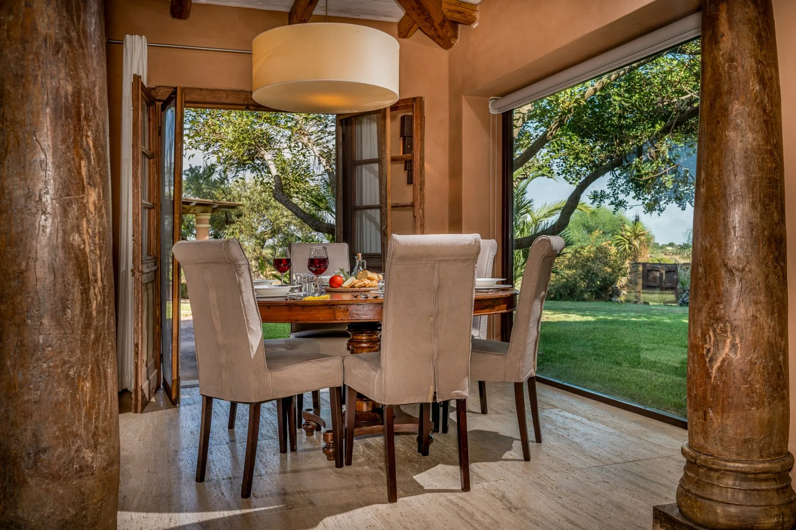 Un comedor con asientos tapizados junto a grandes ventanales que dan a un jardín.