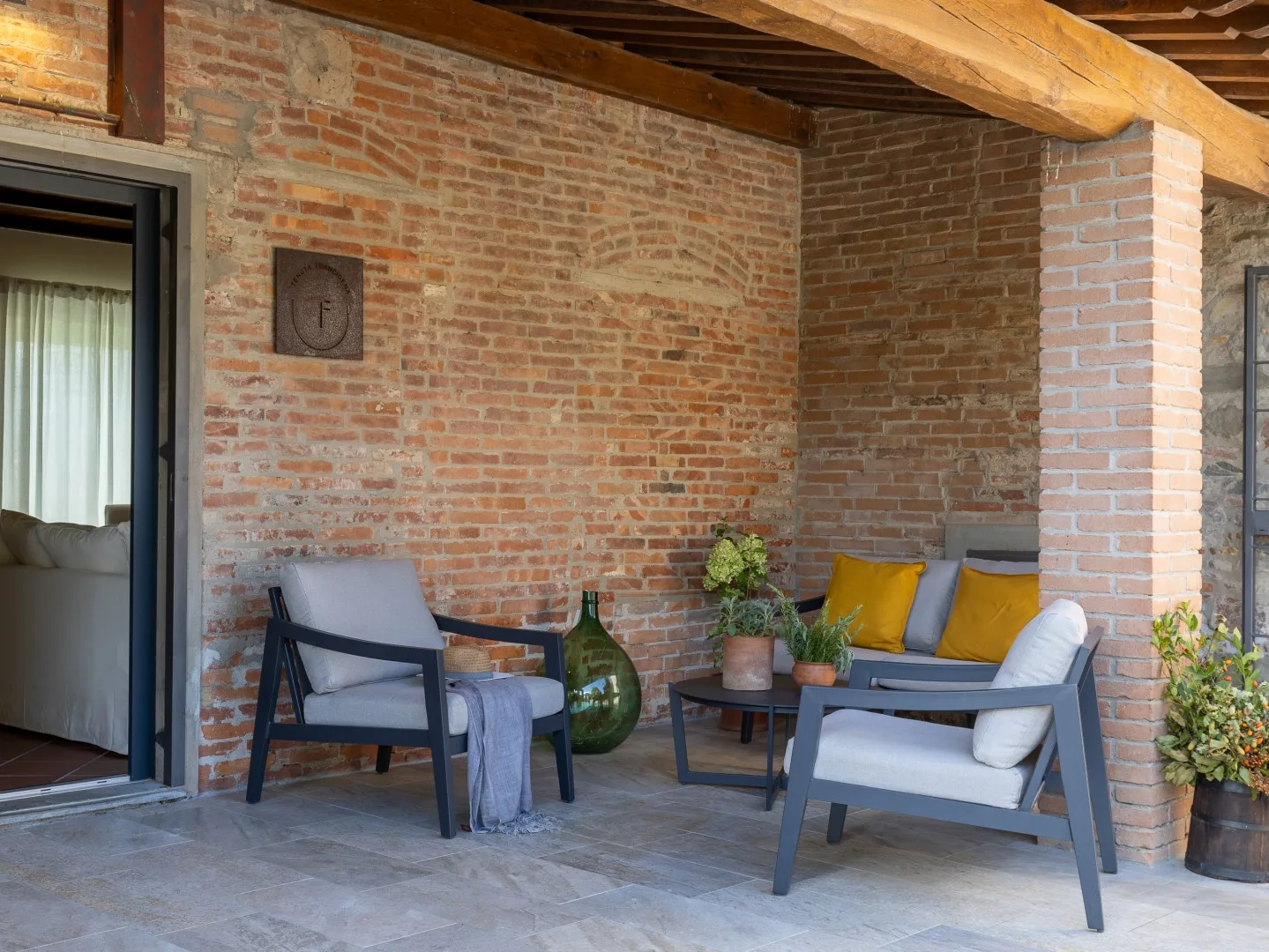 Una zona de estar en un patio de ladrillo con sillones acolchados y plantas en macetas.