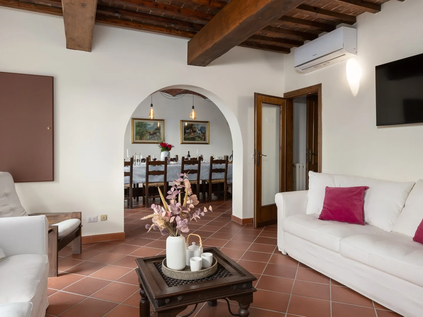 Una sala de estar con asientos blancos y una mesa de centro, abierta a un comedor.