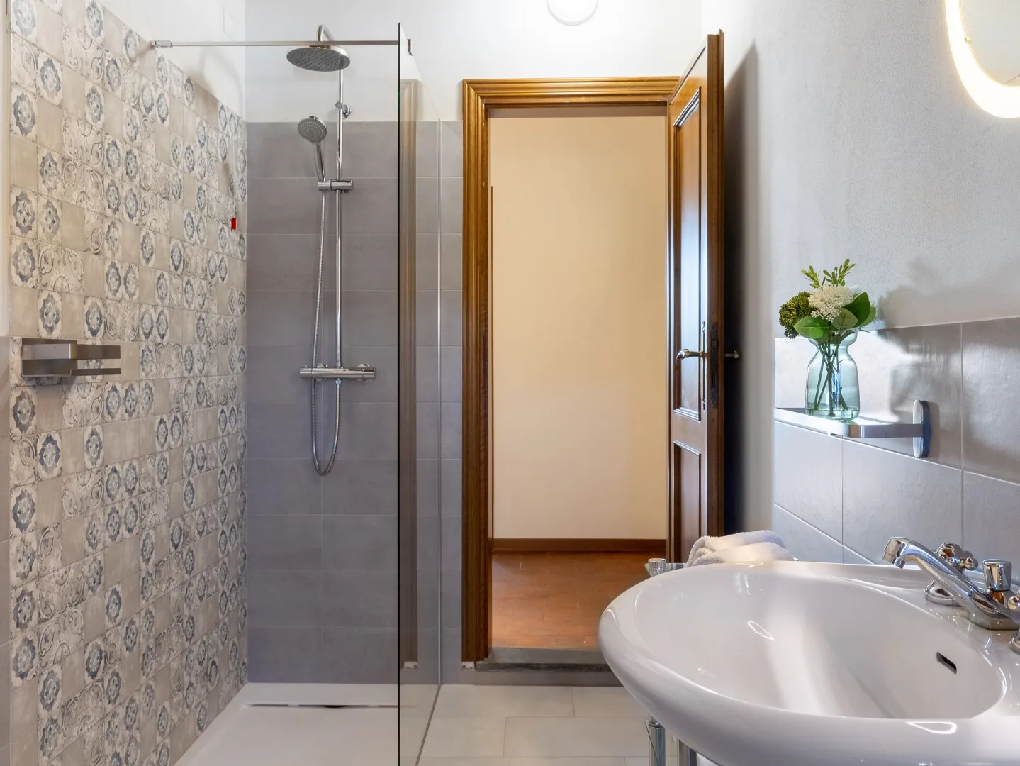 Un baño con ducha de cristal, azulejos estampados y lavabo.