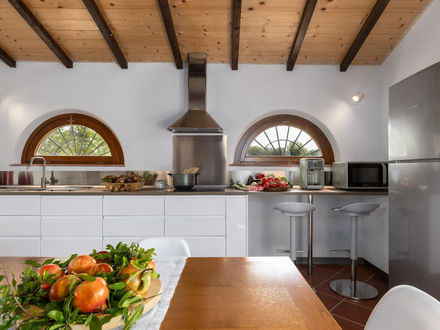 Una cocina luminosa con una mesa de madera y ventanas arqueadas.