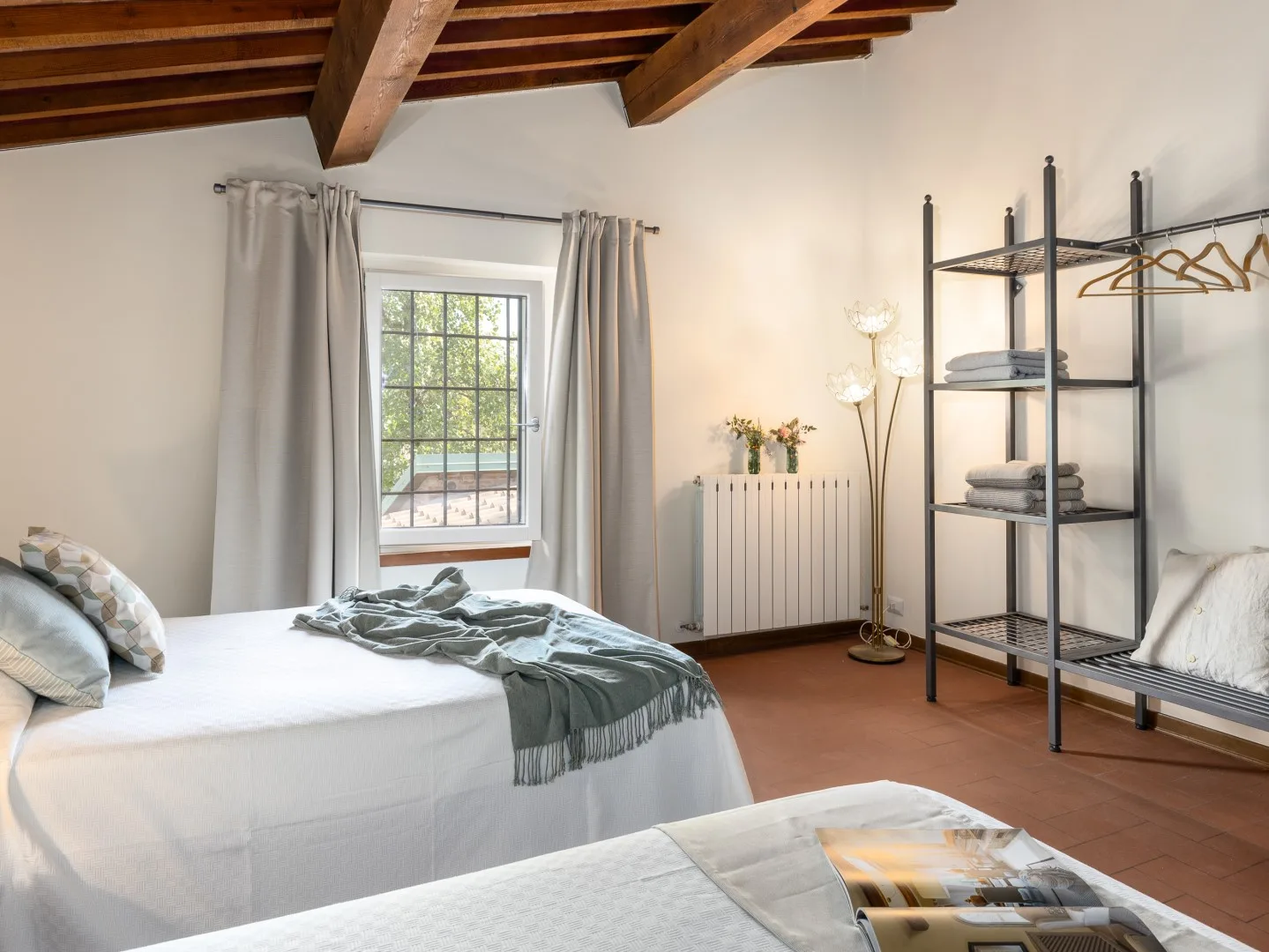Un dormitorio con una cama, una ventana y estanterías abiertas bajo vigas de madera vistas.
