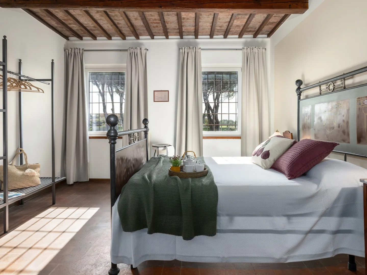 Un dormitorio con una cama bajo vigas de madera vistas y dos ventanas con cortinas.