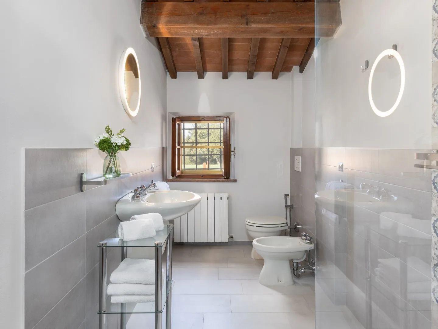 Un baño luminoso con lavabo, inodoro y ventana bajo un techo de madera.