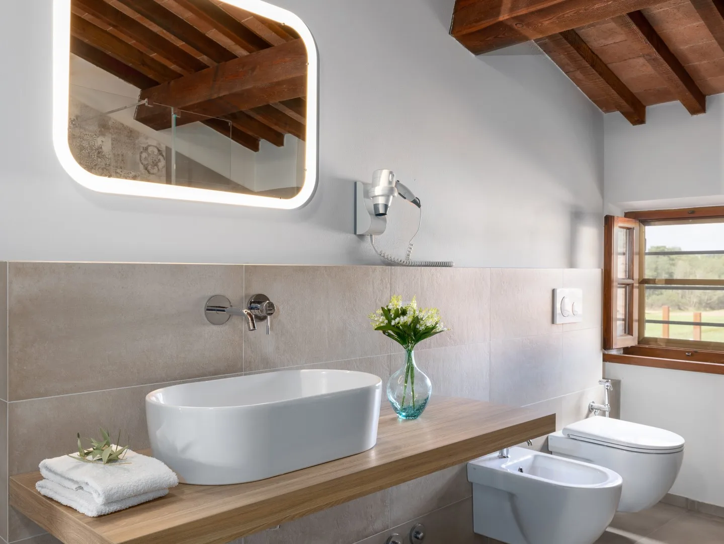 Un baño con lavabo sobre encimera, inodoro y vigas de madera en el techo.