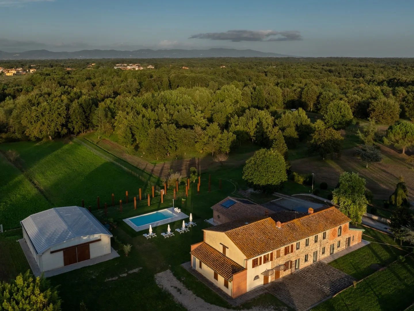 Vista aérea de una propiedad rural con una casa grande, piscina y bosque alrededor.