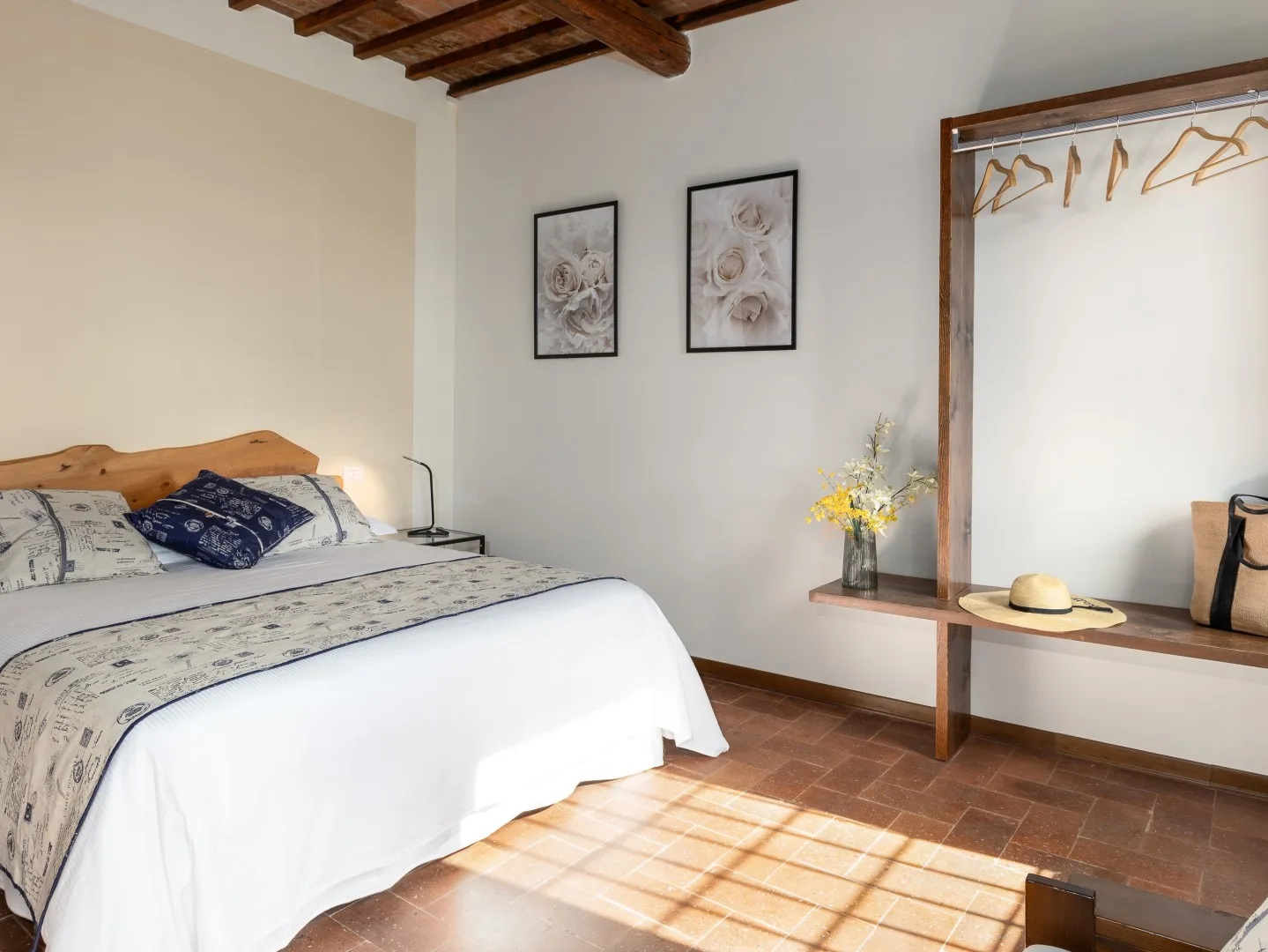 Un dormitorio con una cama, cuadros florales y un perchero abierto.