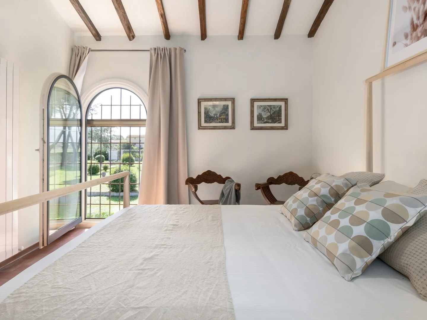 Un dormitorio luminoso con una cama, almohadas estampadas y una ventana arqueada.