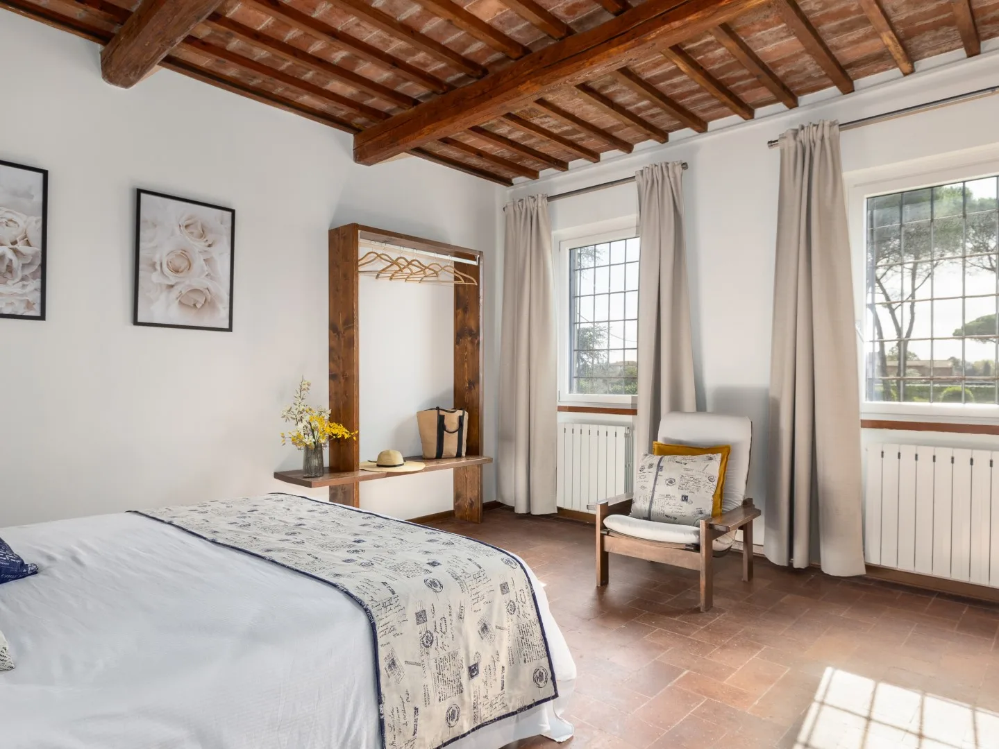 Un dormitorio luminoso con una cama, una silla de madera y ventanas grandes.
