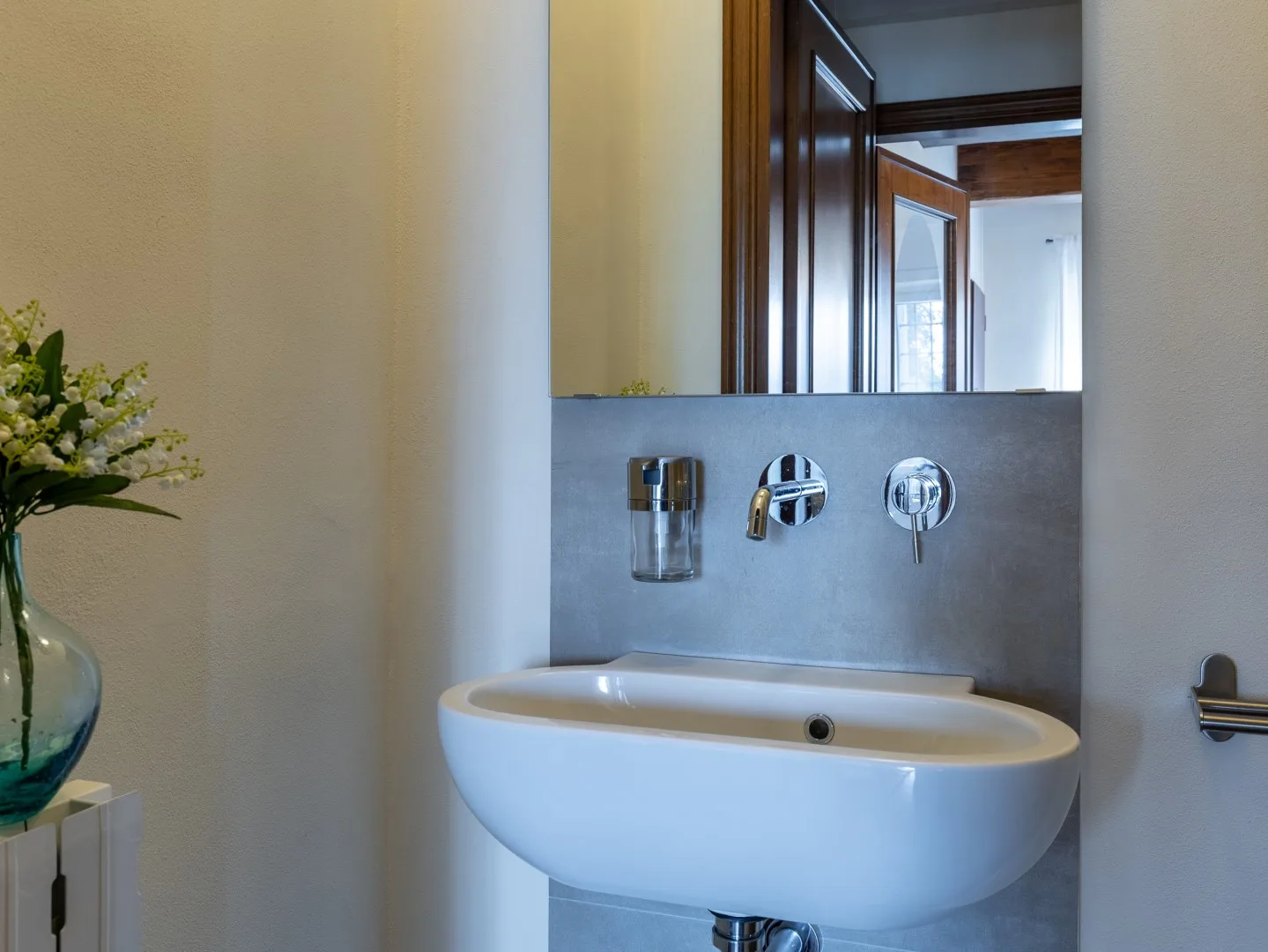 Un lavabo de baño con una cuenca blanca, grifería de pared y un espejo.