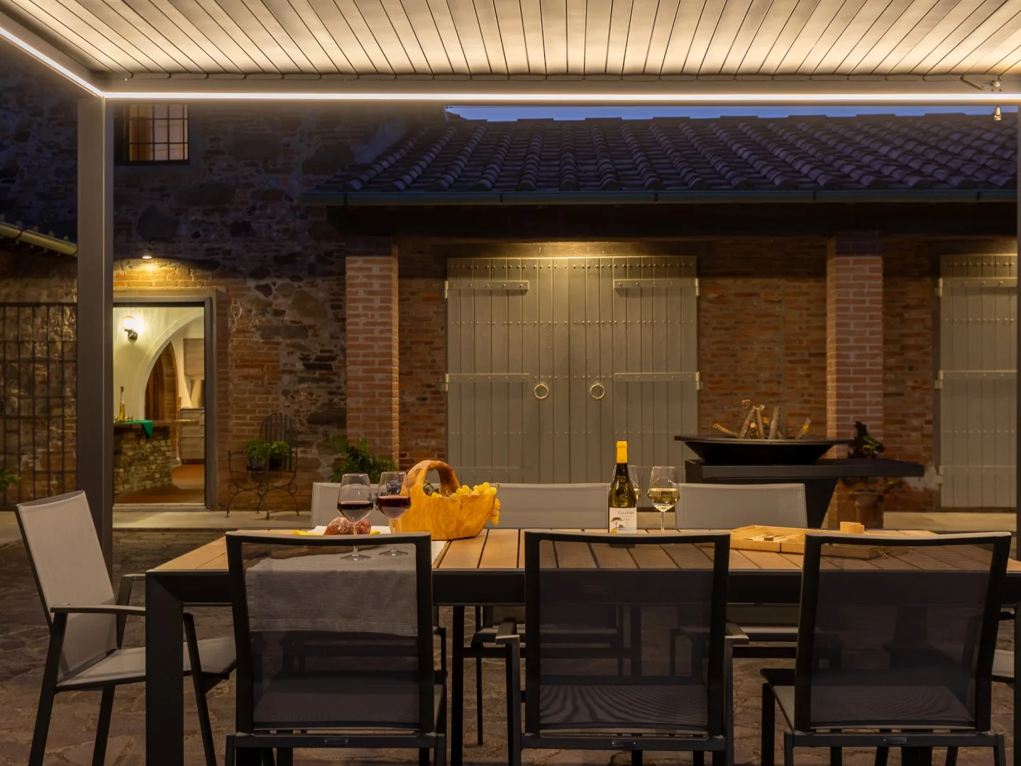 Comedor exterior cubierto con una mesa larga y sillas oscuras de malla.