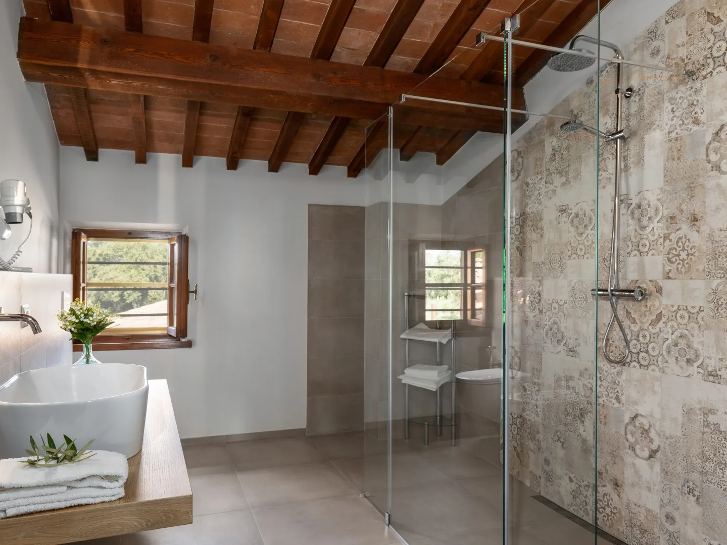 Un baño luminoso con ducha de vidrio, bañera y vigas de madera a la vista.