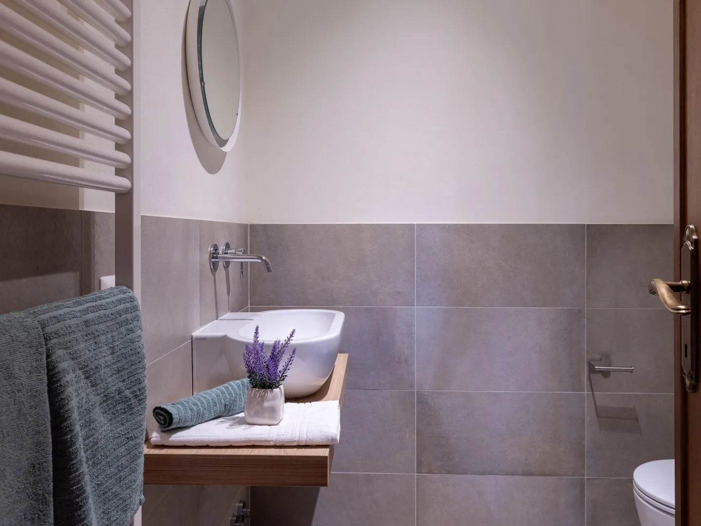 Un baño con un lavabo de pared y paredes revestidas de azulejos grises.