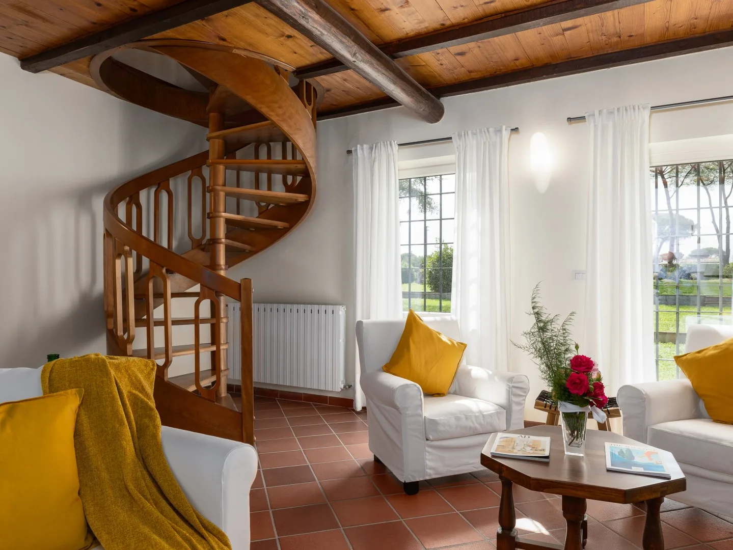 Una sala luminosa con una escalera de caracol, asientos blancos y grandes ventanas.