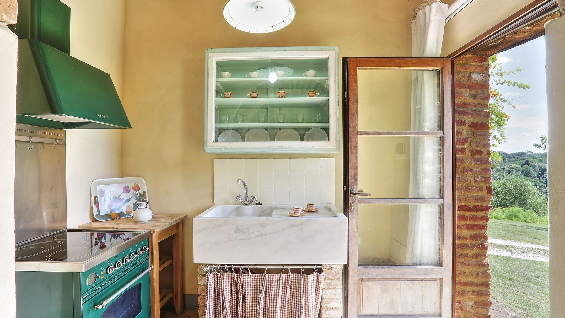 A compact kitchen with a sink, green stove, and open glass door.