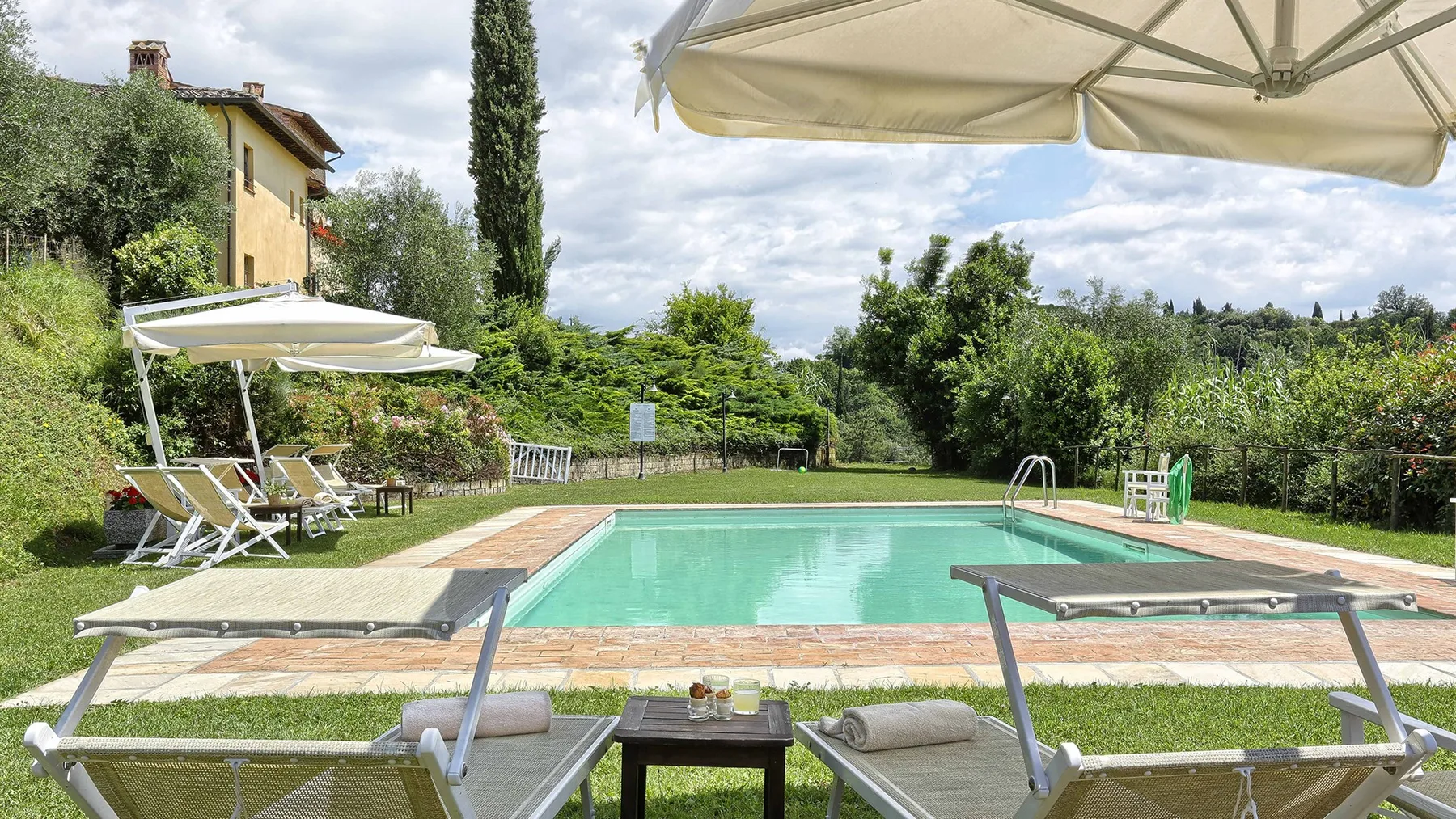 An outdoor swimming pool is surrounded by lawn, loungers, and greenery.