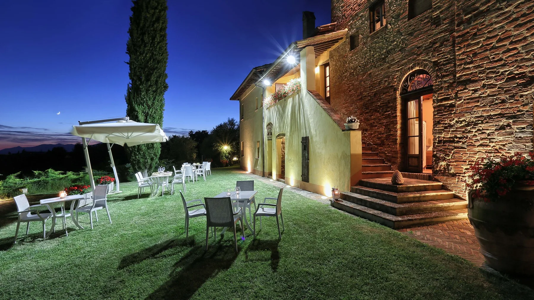 A stone building opens onto a grassy outdoor seating area beneath the evening sky.