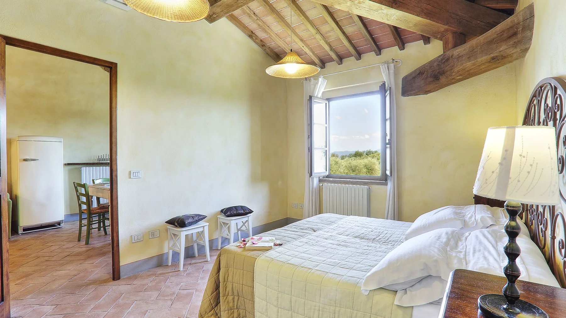 A bedroom with a bed beneath exposed wooden ceiling beams and a window.