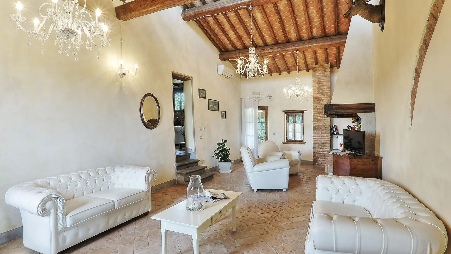 A living room with white seating, a coffee table, and exposed wooden ceiling beams.