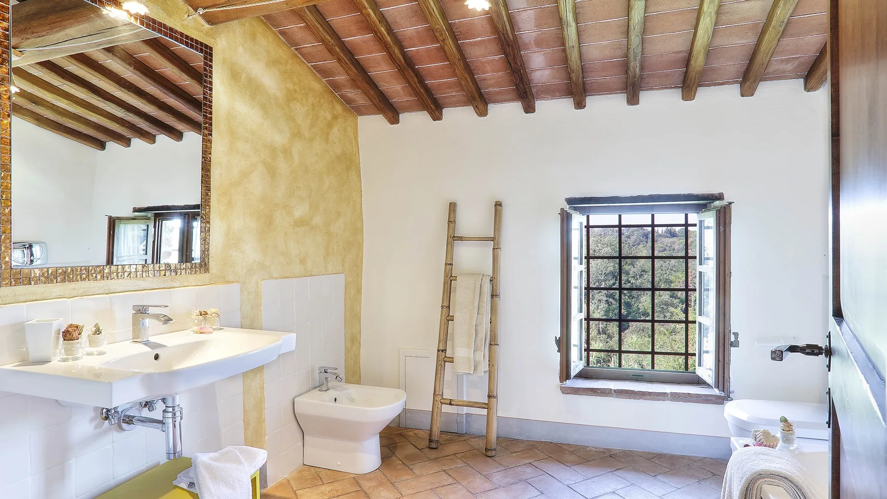 A bright bathroom with a sink, toilet, and a window beneath exposed ceiling beams.