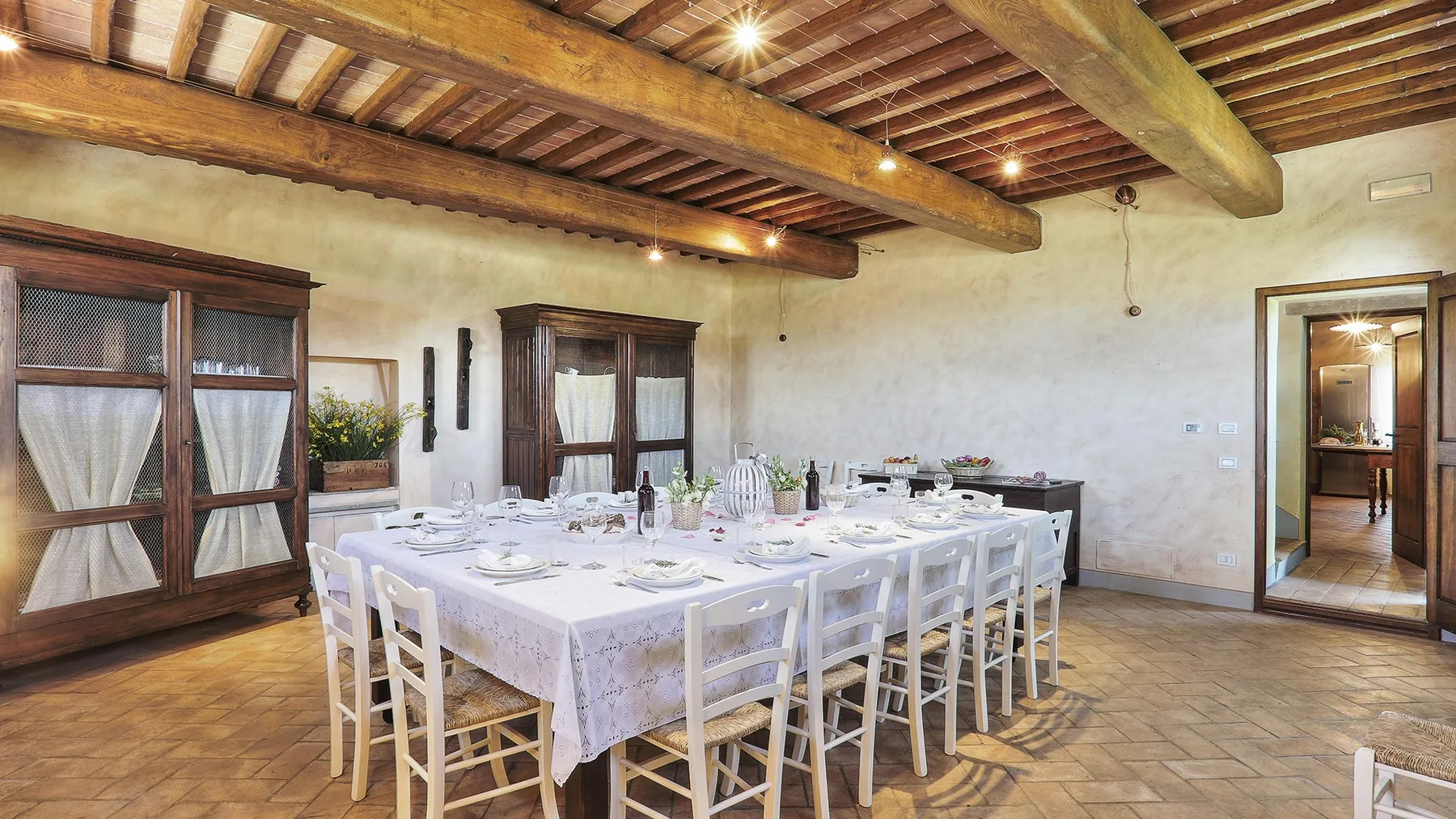 A dining room arranged with a long table and place settings beneath exposed wooden beams.