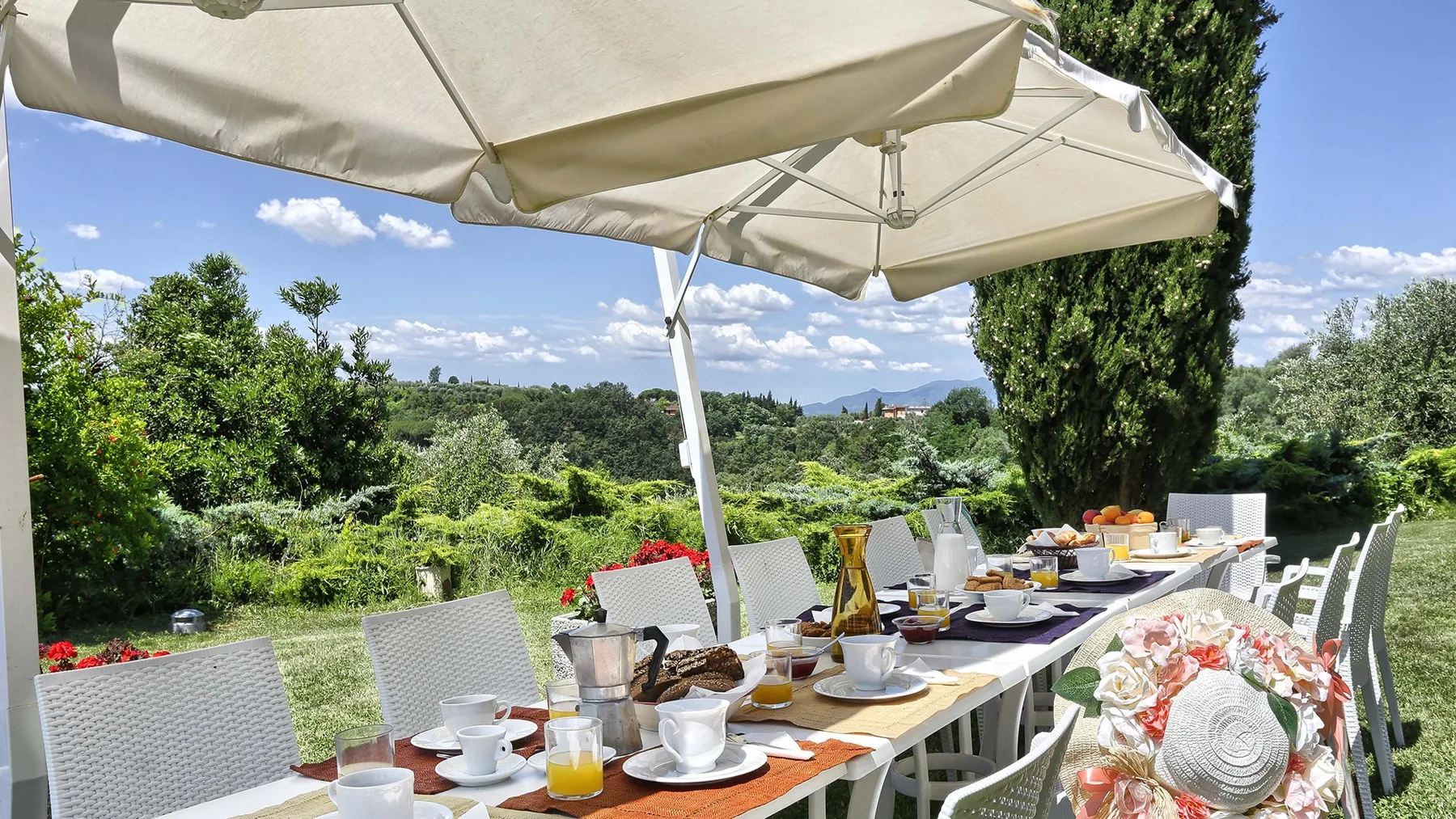 An outdoor dining table sits beneath large umbrellas amid lush greenery.