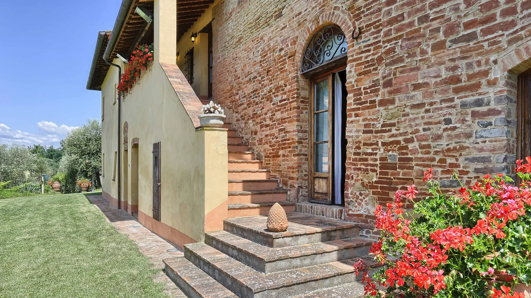 A brick building entrance opens onto stone steps beside a grassy garden.