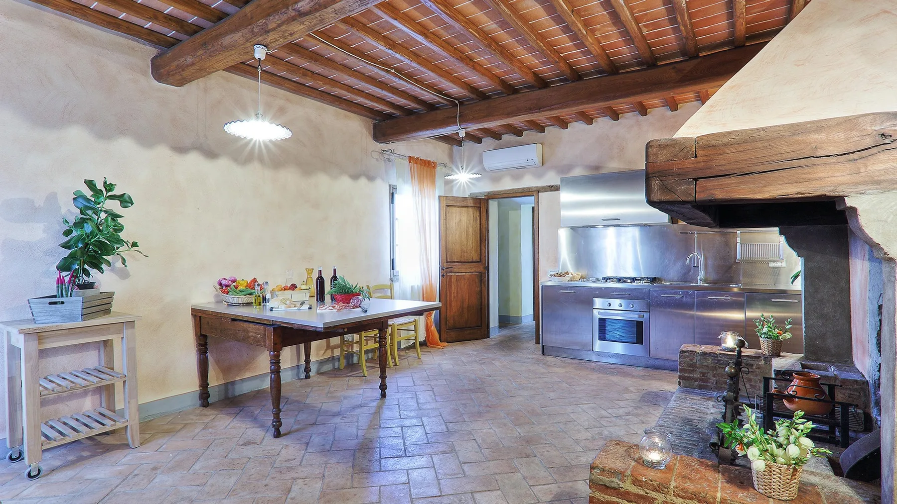 A rustic kitchen and dining area with a wooden table beneath exposed ceiling beams.