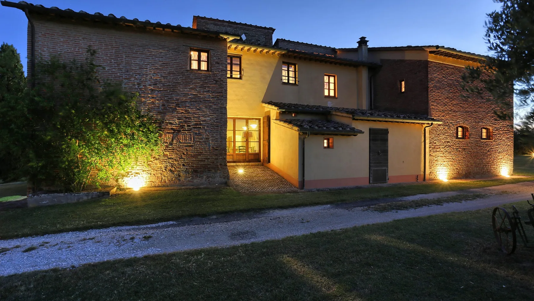 A brick house exterior at dusk, illuminated by warm outdoor lights.