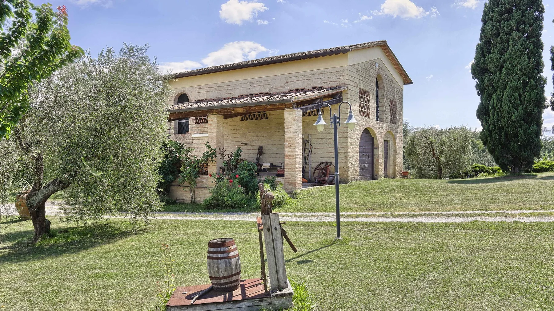 A stone house stands beside a grassy yard with trees and a wooden well structure.