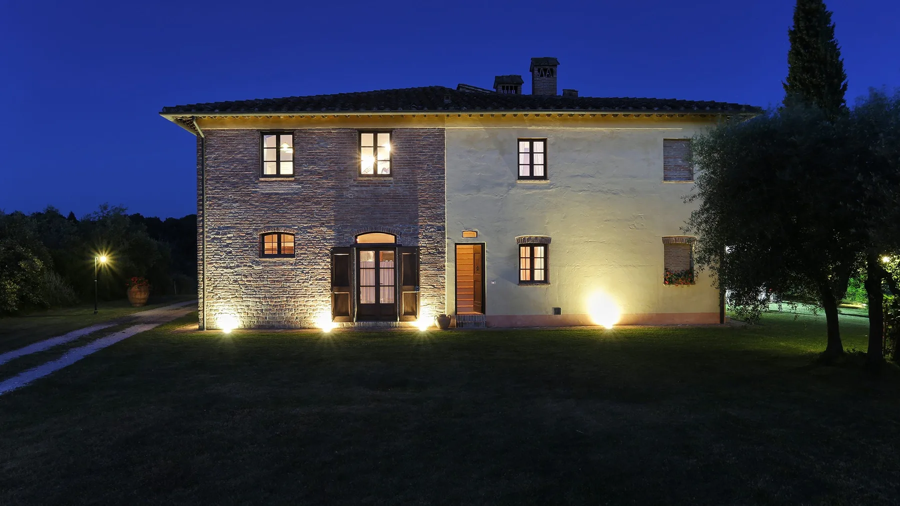A two-story house at night, with exterior lights illuminating its facade.