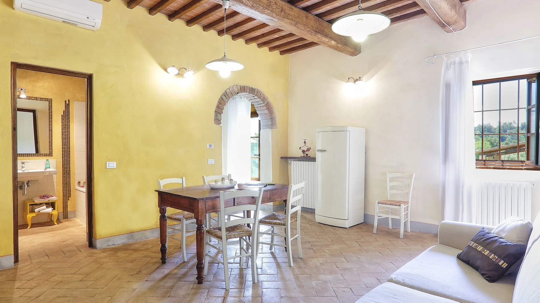 A dining area with a table and chairs beside an arched doorway and a refrigerator.