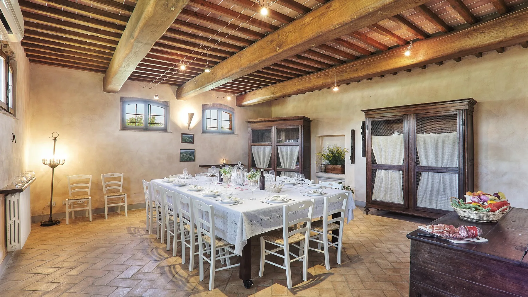 A rustic dining room with a long table set beneath exposed wooden beams.