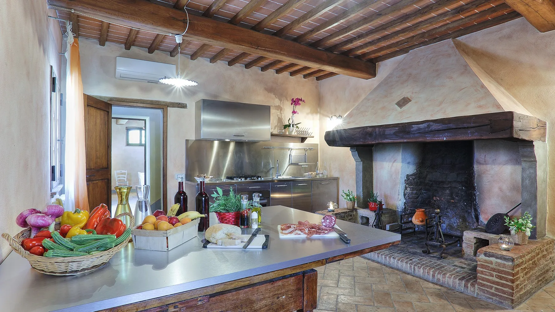 A rustic kitchen with a central island and a large open fireplace.