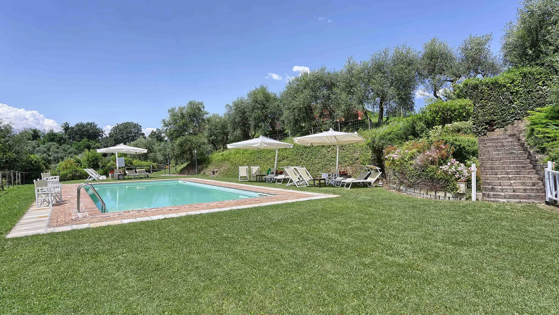 An outdoor swimming pool sits beside a broad lawn, with sun loungers and umbrellas.