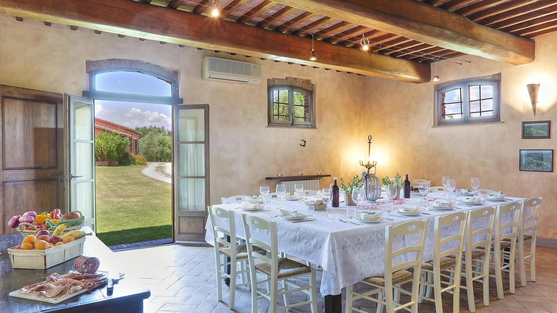 A dining room with a long table set with dishes beneath exposed wooden beams.