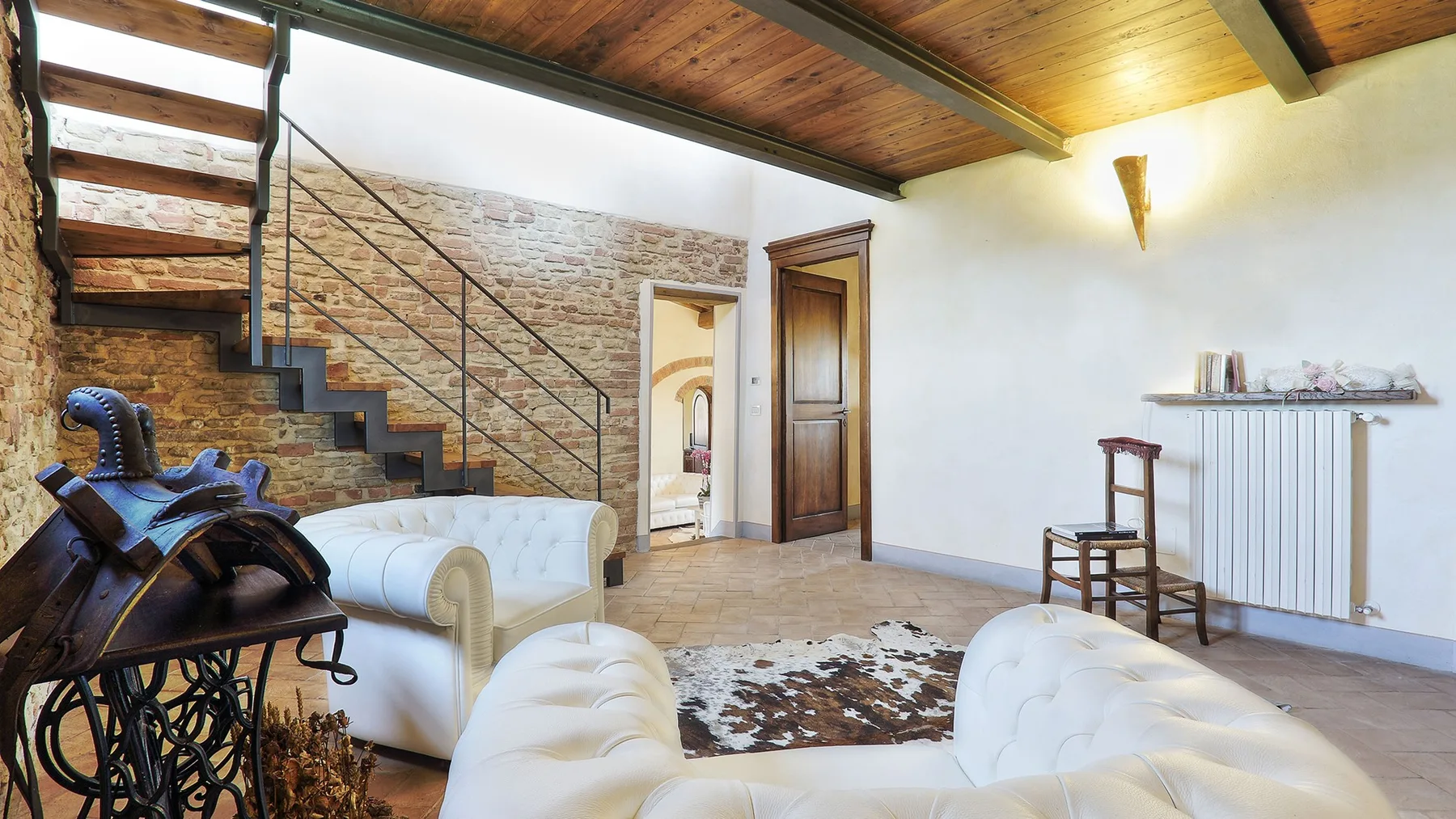 A living room with white seating, a staircase, and a wooden ceiling.