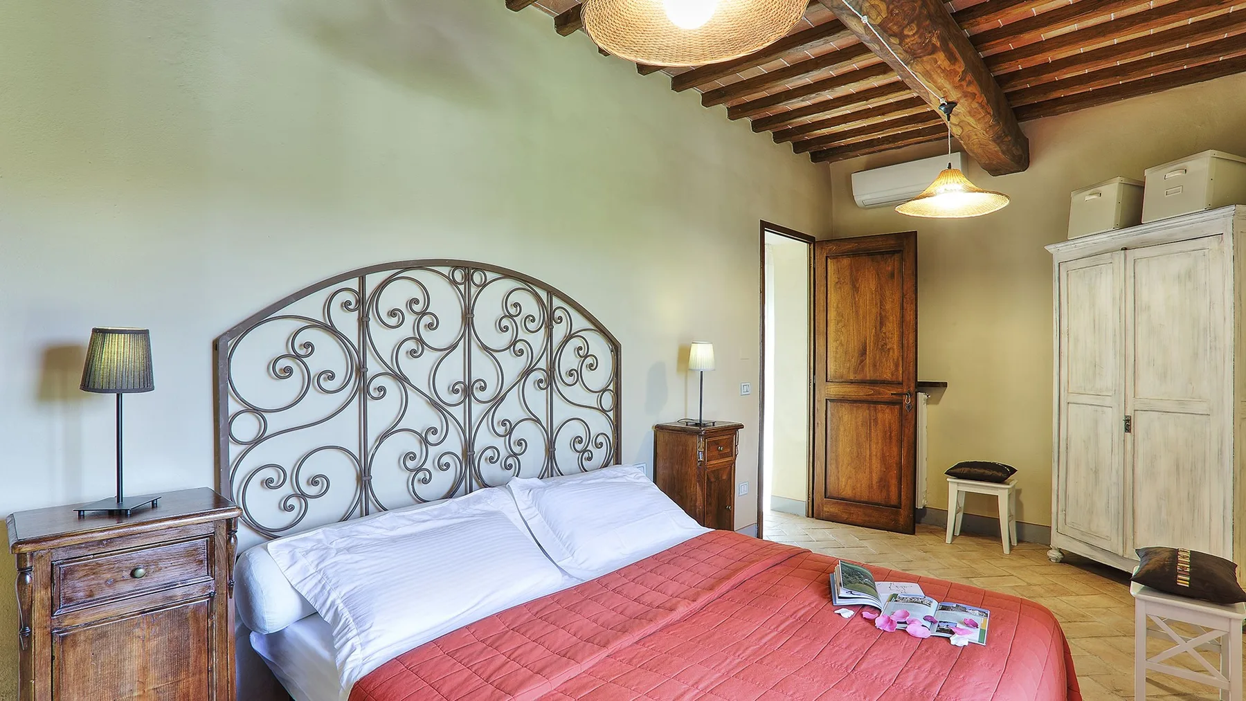 A bedroom with a bed, patterned metal headboard, and exposed wooden ceiling beams.
