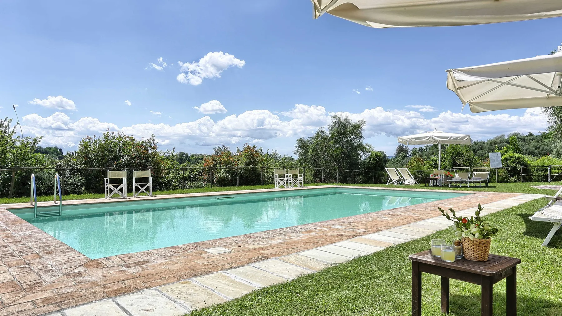 An outdoor swimming pool is surrounded by a paved deck and green lawn.