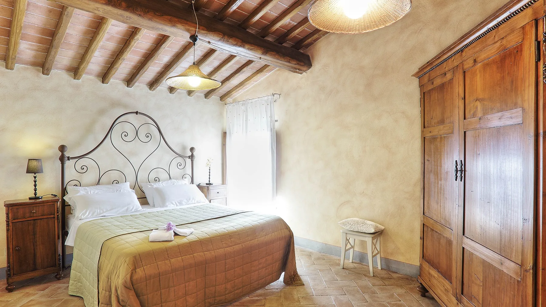 A bedroom with a bed, wooden wardrobe, and exposed ceiling beams.