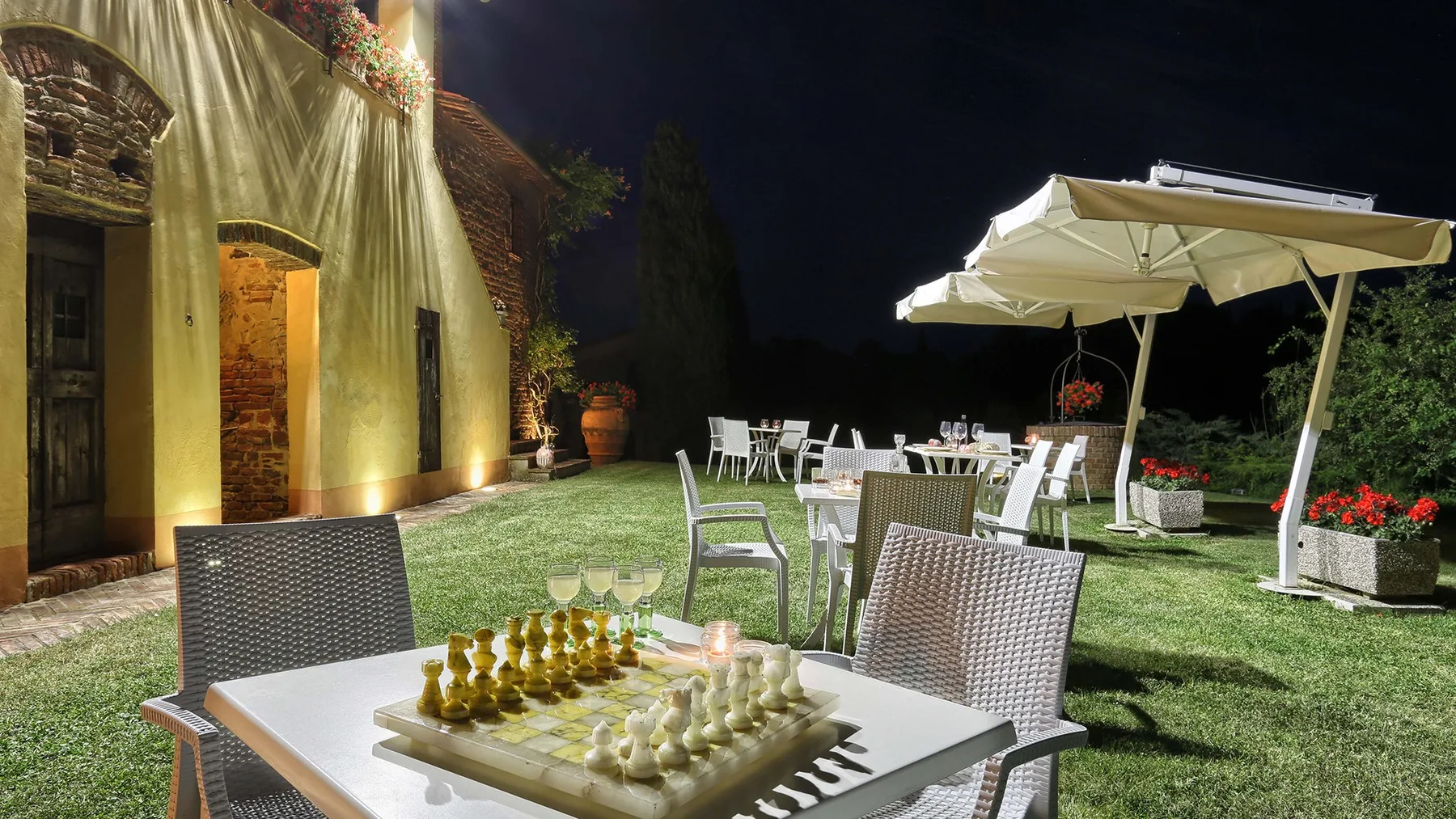 An outdoor dining area at night, with a table set beside a large patio umbrella.