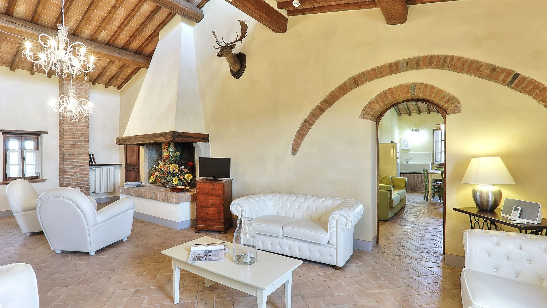A living room with white seating, a fireplace, and exposed wooden ceiling beams.