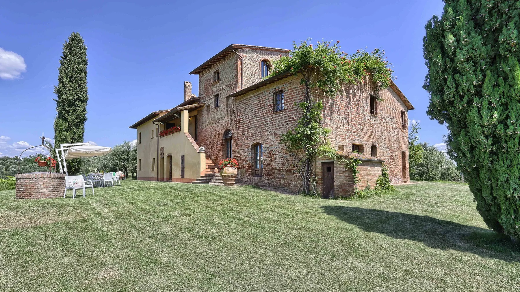 A rustic brick house stands on a grassy lawn beneath a clear blue sky.
