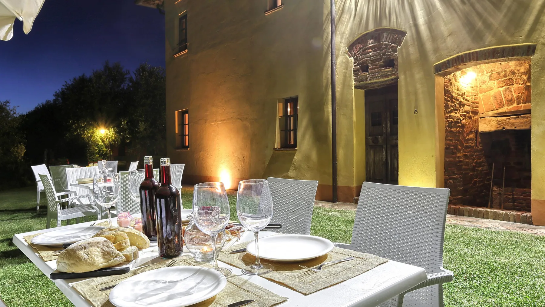 An outdoor dining area with a set table beside a warmly lit building.